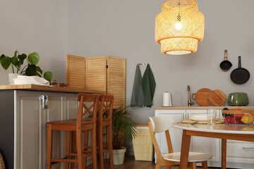Interior of modern kitchen with glowing lamps, dining table and white counters at evening