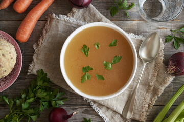 Chicken bone broth or soup in a white plate, top view