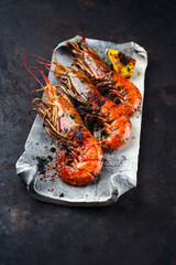 Traditional fried king prawns with pineapple pieces and black salt served as close-up on a design tray with text space