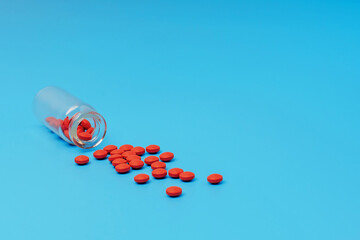 A glass bottle from which red pills are poured on a blue background