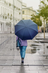 Girl under umbrella walking on wet sidewalk in city