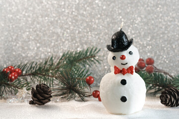 Snowman candle on a silver Christmas background with Christmas tree branches in vintage style. Selective focus. Place for text. greeting card