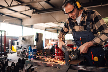 Caucasian worker in a workshop grinding a piece of metal construction.