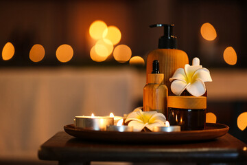 Spa composition with plumeria flowers and burning candles on table in dark salon, closeup