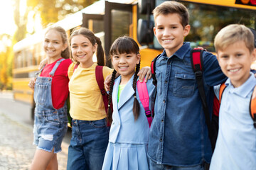 Cheerful kids ready to board school bus, standing outdoors