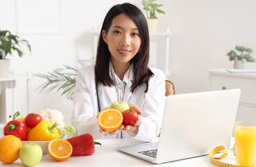 Female Asian nutritionist with healthy food at table in office