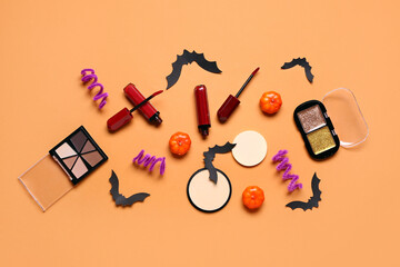 Lipsticks and different decorative cosmetics with Halloween decor on orange background