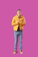 Young man in warm puffer jacket on purple background