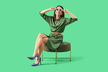 Stylish young Asian woman sitting on green background