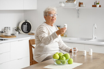 Fototapeta premium Senior woman with pill bottle in kitchen