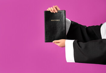 Hands of young Asian nun with Bible on purple background, closeup