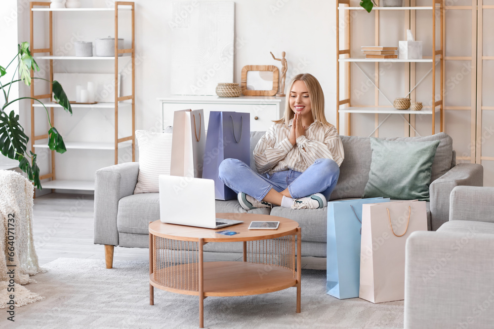 Wall mural Young woman with laptop and shopping bags sitting on sofa at home