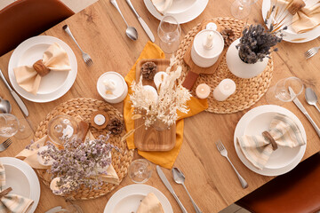 Elegant table setting with dried flowers, burning candles and pine cones