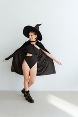 Dancing young happy sexy woman in black witch hat with shopping bags after successful shopping. Halloween sale, discounts