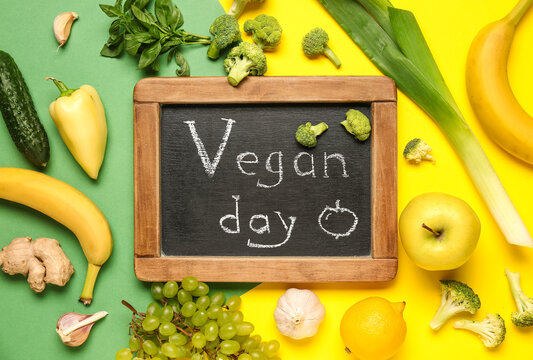 Chalkboard with word VEGAN DAY, fresh vegetables and fruits on color background