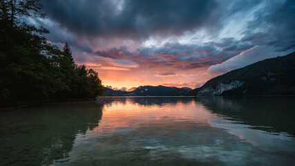 Sunset over the alpine lake Wolfgangsee with storm clouds and an alpine village in the background....