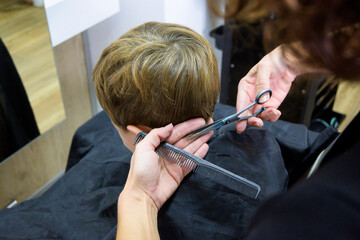 A little cute boy sits in a hairdresser's at the stylist's, a schoolchild is getting hair cut in a...