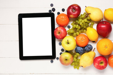 Tablet computer and fresh fruits on white wooden background. World Vegan Day concept