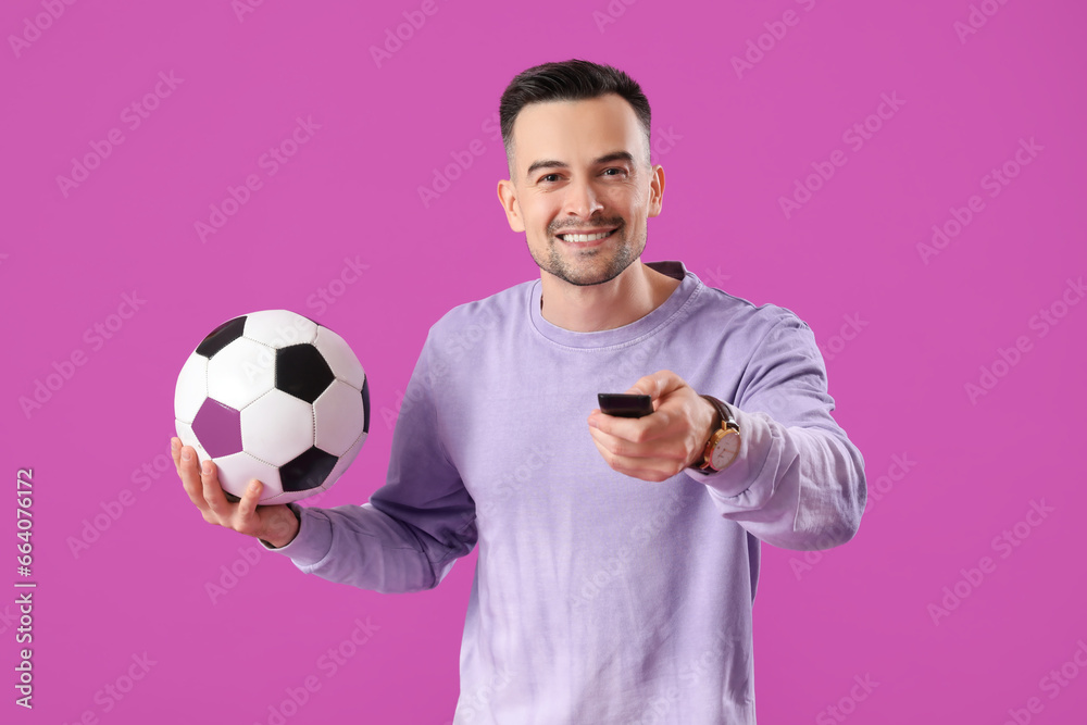 Poster happy young man with soccer ball and tv remote control on purple background