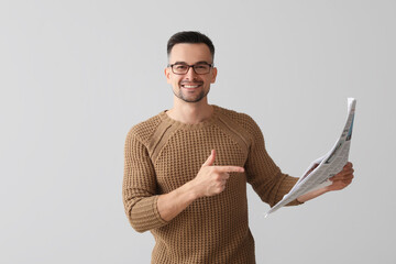 Happy young man pointing at newspaper on light background