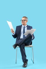 Mature actor reading film script in chair on blue background