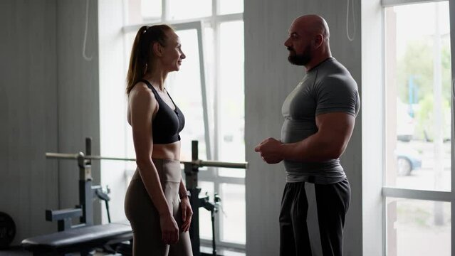 A man fitness trainer and a girl client in the gym have contented conversation after finishing a workout. A girl athlete and coach happily discuss victory or a prize place in competition. Sportswoman