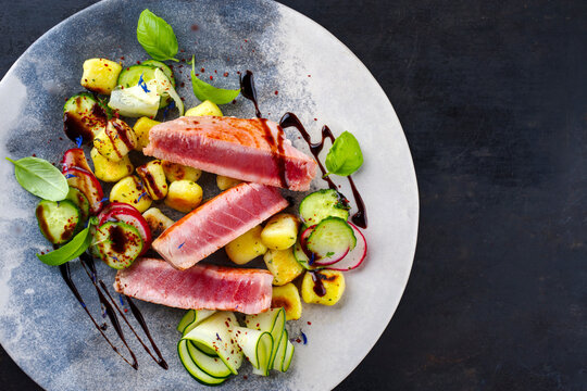 Traditional Italian fried tuna fish steak with gnocchi and cucumber slices served as top view on a Nordic design plate with copy space right