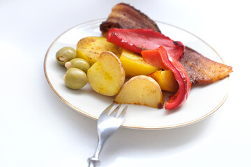 oven grilled bacon slices with delicious curry sauce served on white plate, baked potatoes with meat, red paprika, green capsicum, ripe tomatoes, spices, junk food concept, traditional family party
