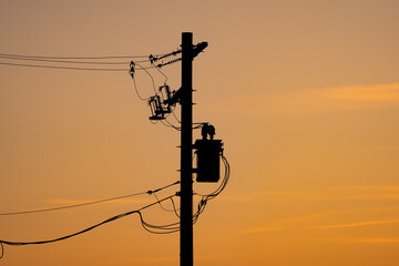Power pole silhouette with resistors and transformers on a power grid under a sunset sky in Alberta Canada.
