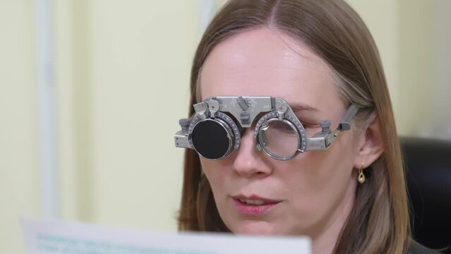 Middle-aged woman reads in glasses for eye exam in ophthalmologist's office.