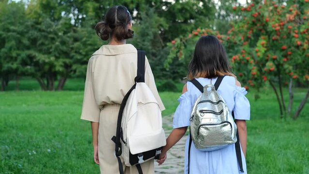 Two girls walking in the park in the summer, talking, walking after school and college, holding hands, best friends, sisters returning home after school