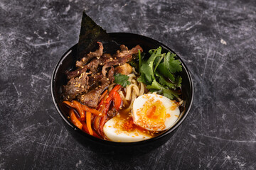 Rice bowl with beef, noodles, egg and vegetables on a dark background