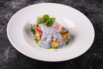 grilled tuna with greens on a white plate on a dark background