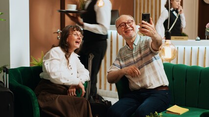 Elderly tourists using videocall connection to keep in touch with family members, travelling together on retirement trip. Husband and wife talking to children on teleconference call. Tripod shot.