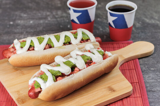 complete italian: on wooden table and poly paper cups of national holidays, with chilean flag. tomato, mayonnaise, vianesa, palta and mustard on hot dog bread, on a table. Typical chilean food concept