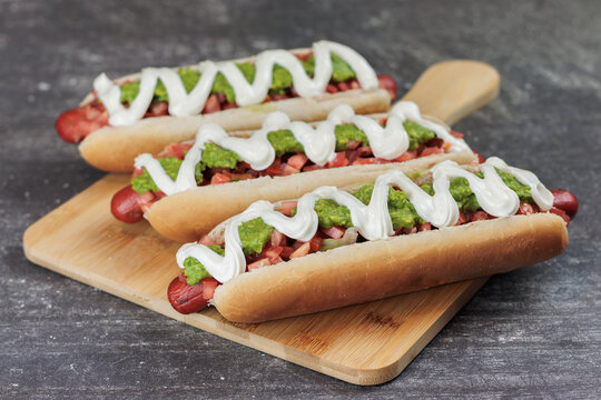 completo italiano: on wooden board, tomato, mayonnaise, vianesa, palta and mustard on a hot dog bun, on a table. Typical Chilean food concept