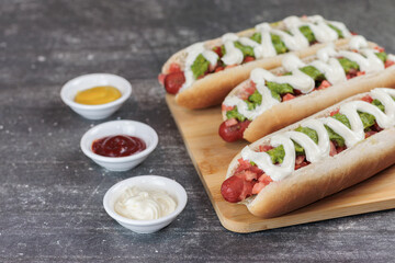 completo italiano: on wooden board, bowls with moztaza, mayonnaise and ketchup. vianesa, palta on hot dog bun, on a table. Left copy space. Typical Chilean food concept