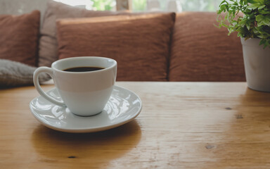 Beautiful cup of cappuccino on the table in front of sofa in modern house with plants and nice view.