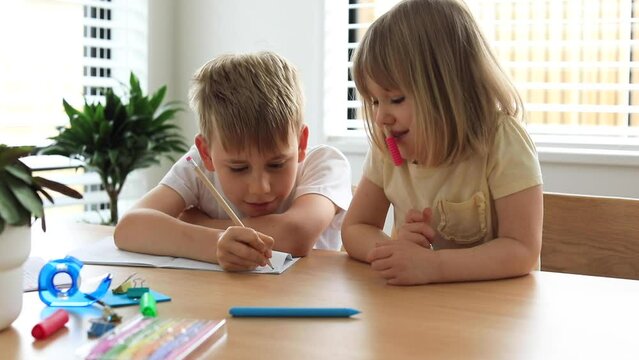 Brother and sister write and draw together with pencils at the table. 
