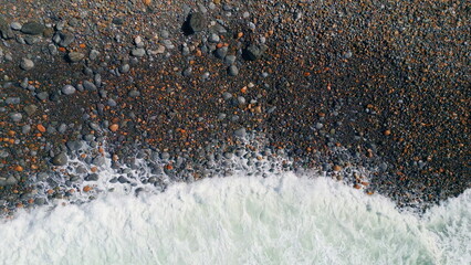 Foamy sea water washing volcanic beach stones aerial view. Ocean foam rolling 