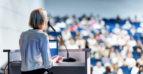 Female speaker giving a talk on corporate business conference. Unrecognizable people in audience at conference hall. Business and Entrepreneurship event