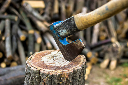 Old axe standing against a piled pieces of firewood stucked in tree stump
