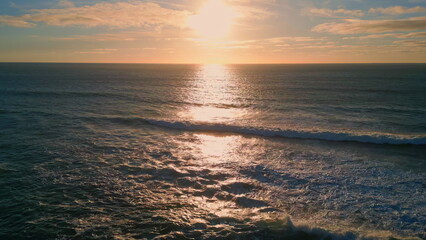 Golden sunset sky rippling ocean surface drone view. Sea reflecting sunlight