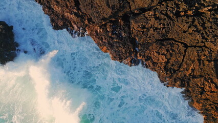 Top view foaming ocean hitting coastal rock making bubbling foam in slow motion