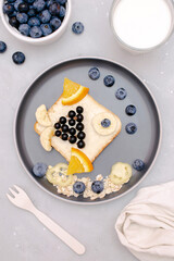 Funny cute fish shape sandwich toast bread with blueberry,great bilberry,orange,milk,honey.Kids childrens baby's sweet dessert healthy breakfast lunch food art on plate,gray background,top view