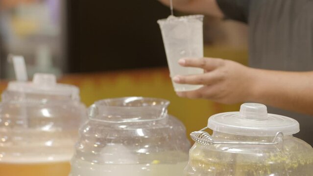 This close up video shows anonymous hands of a vendor serving agua frescas juices with a ladle spoon into cups.