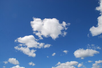 Lake under a cloudy sky. Forest lake with small waves on the surface, under a light blue sky with white cumulus and cirrus clouds. A forest with green foliage grows along the shores of the lake.