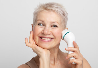 Beauty face portrait of cute and pretty senior woman with short hair using facial massager for...