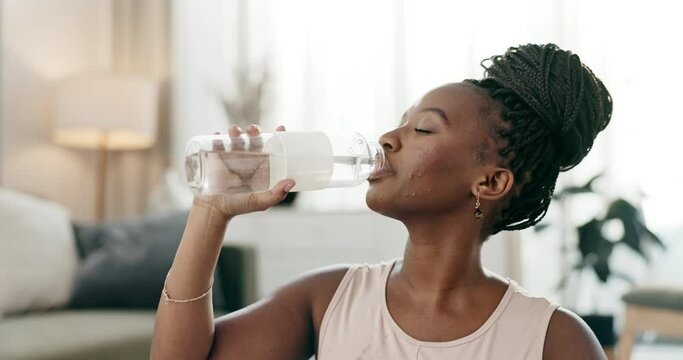 Exercise, black woman and drinking water in bottle in home, healthy diet or wellness. African athlete, thirsty or liquid for hydration after workout, sport training or fitness to relax in living room