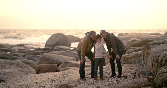 Family, learning and child with shells at the beach with a sunset on the ocean and game on vacation. Mature, man and woman bonding with kid to show a rock, stone or fossil from the sea or water